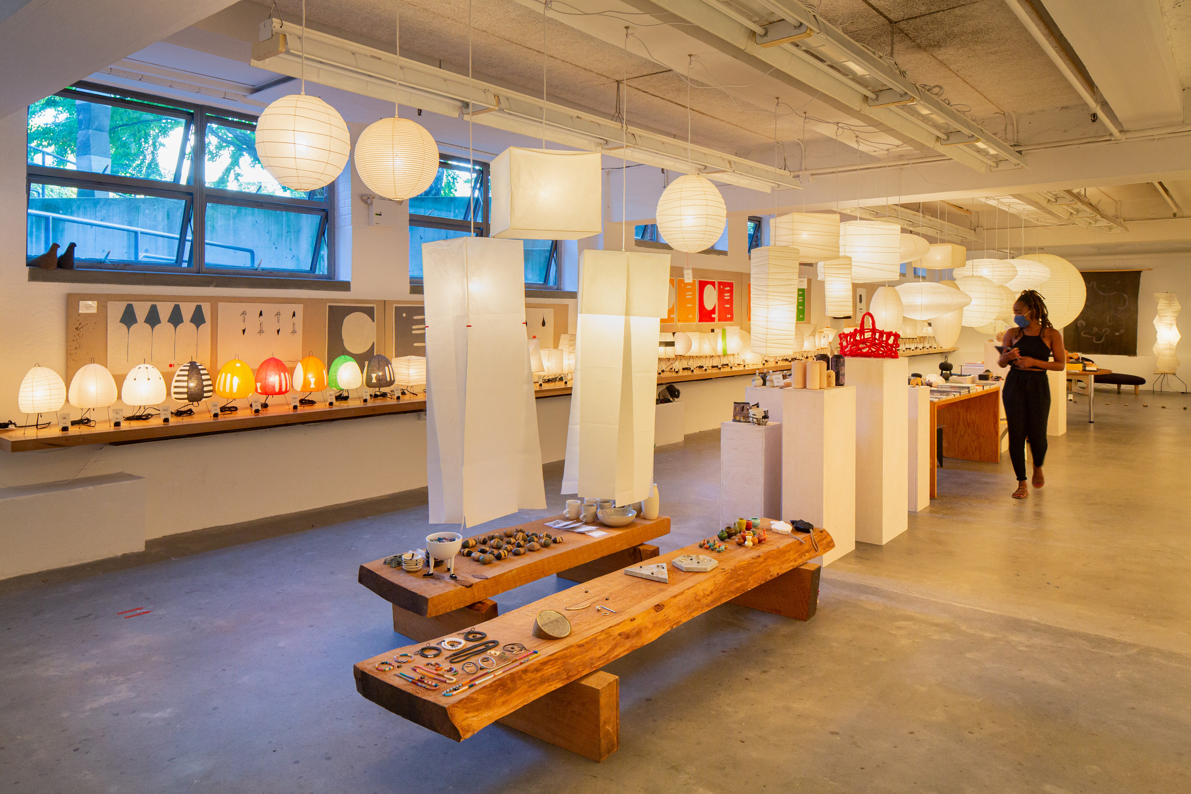 A guest browses the Noguchi Museum Shop wearing a mask. Dozens of Akari lanterns are hung above...