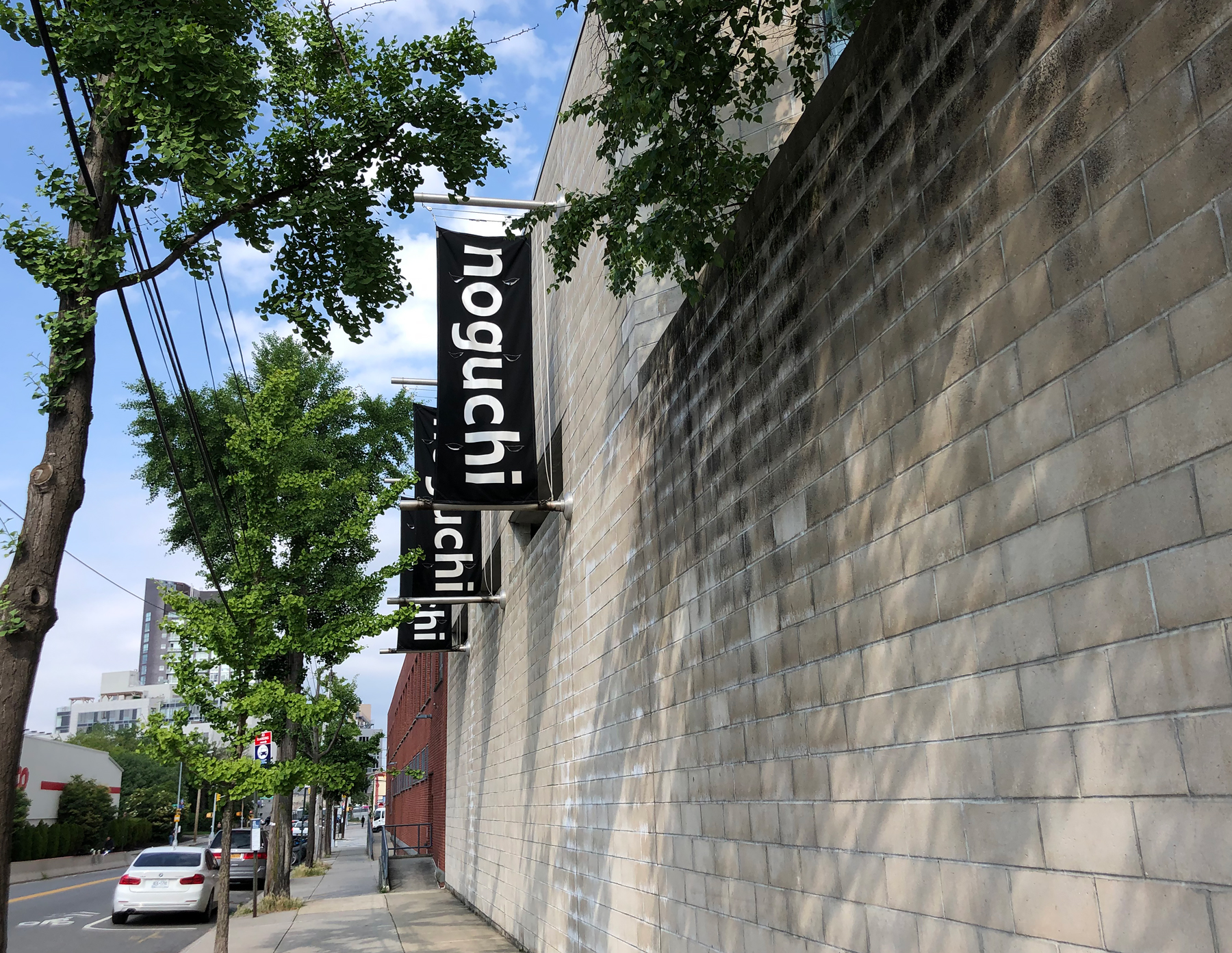 Exterior of Noguchi Museum with three vertical noguchi logo banners on black backgrounds
